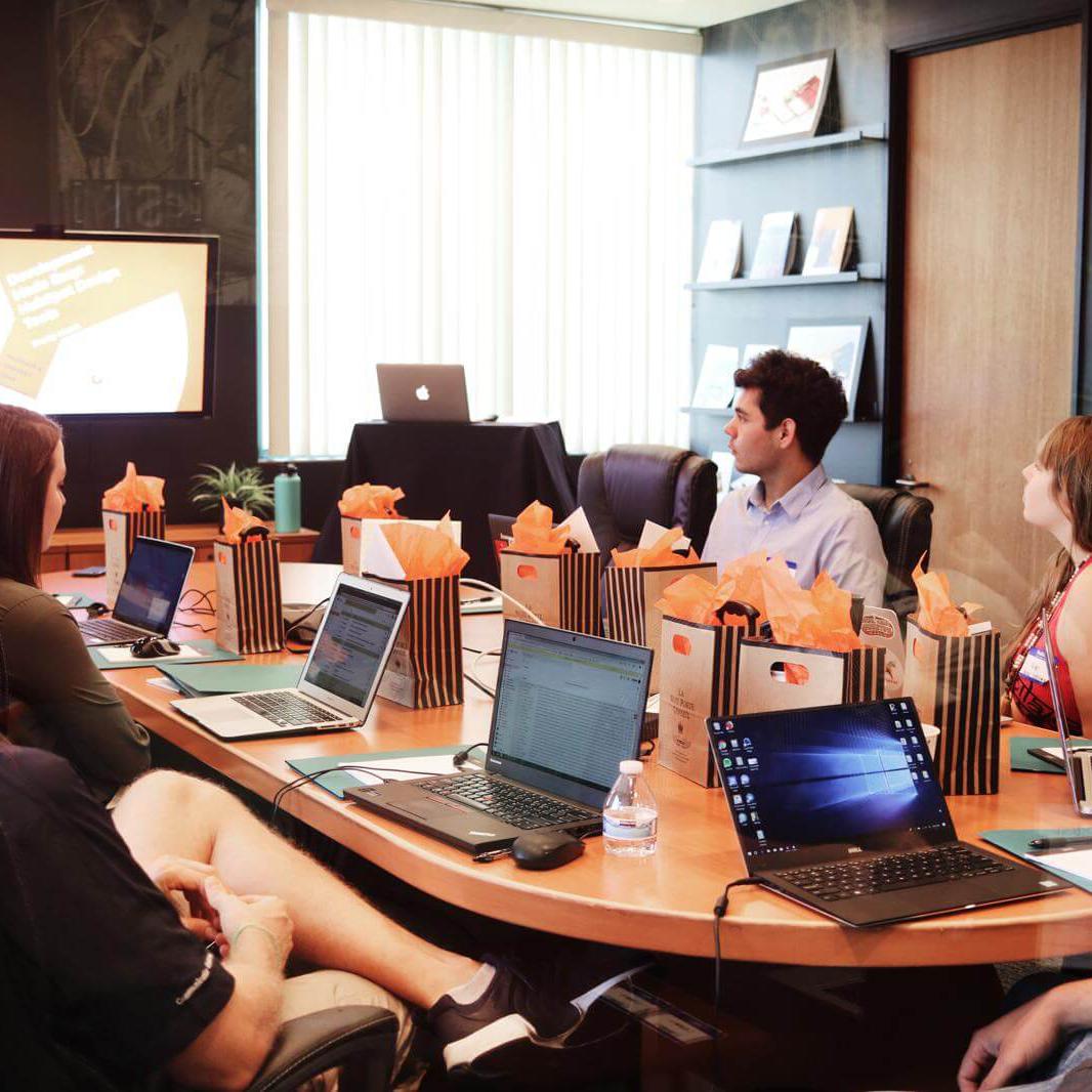 Man standing in front of people sitting beside table with laptop computers